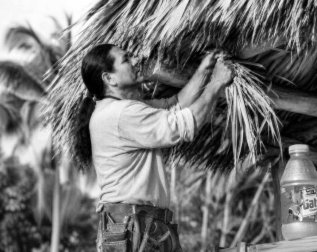 Chief Bobbie tying thatch onto a tiki hut roof