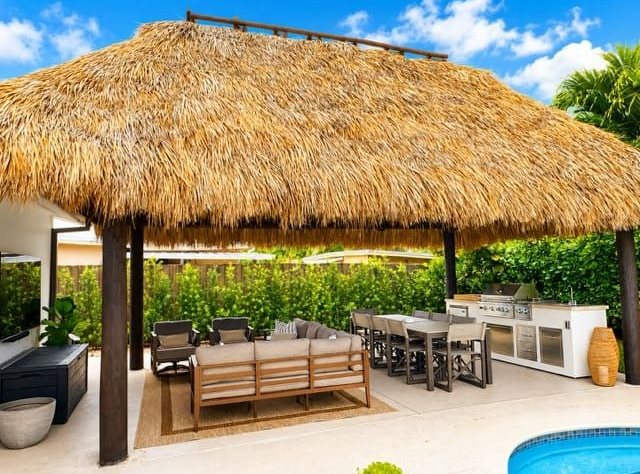 Large thatched hut over an outdoor kitchen and lounge beside a pool