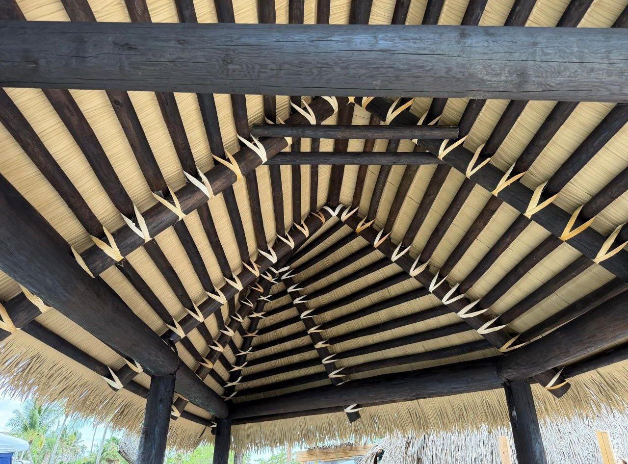 Close-up of the underside of a thatched roof showing cypress rafters and tied thatch